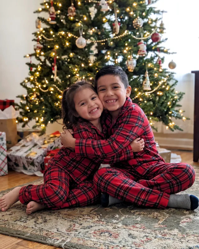 Photo d’un frère et d’une sœur en pyjama devant le sapin