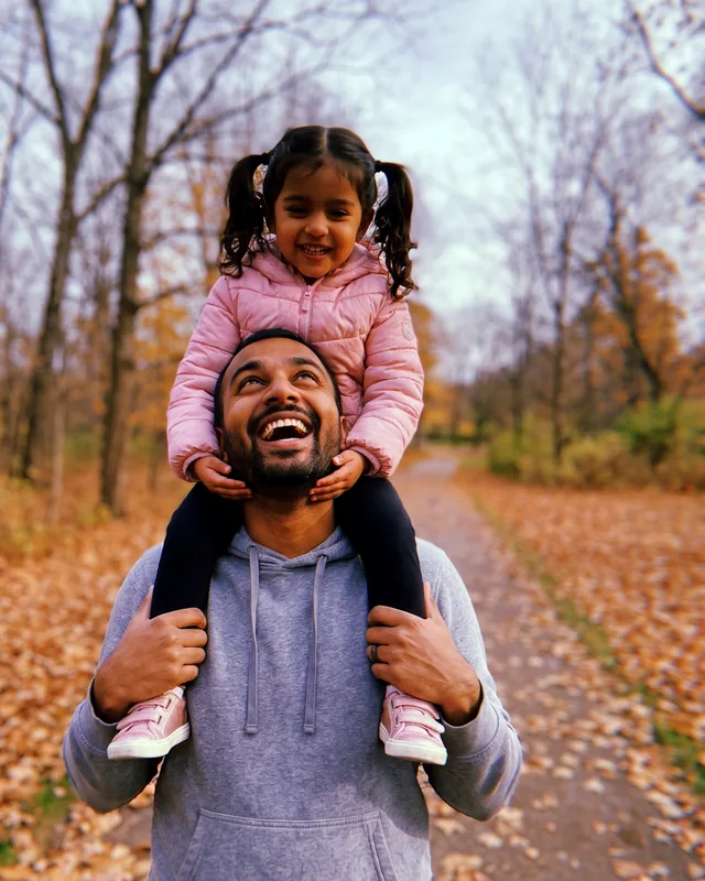Photo d’un père qui porte sa fille sur ses épaules dans un parc en automne